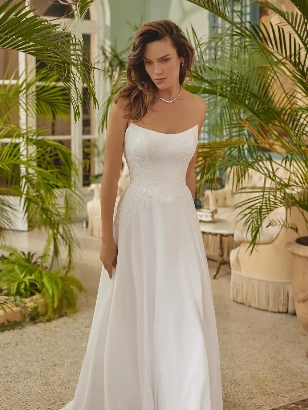 A woman in a white wedding dress stands in a tropical setting with greenery around her.