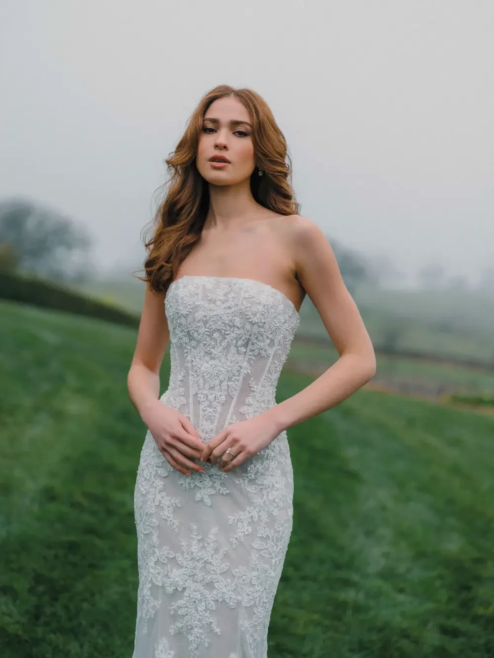 A woman in a strapless wedding dress standing in a foggy outdoor setting.