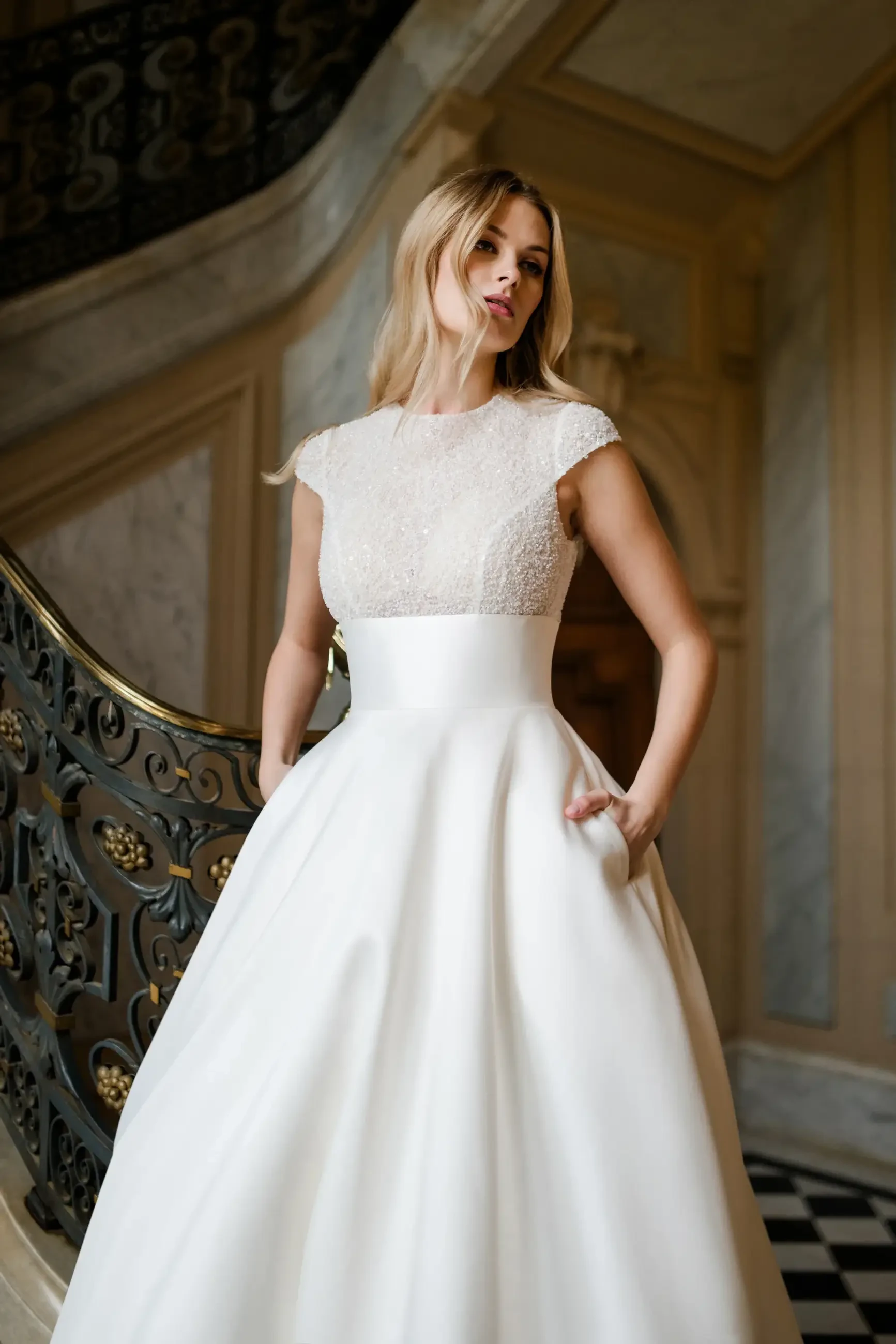A woman in a white wedding dress with intricate detailing, standing elegantly on a staircase.