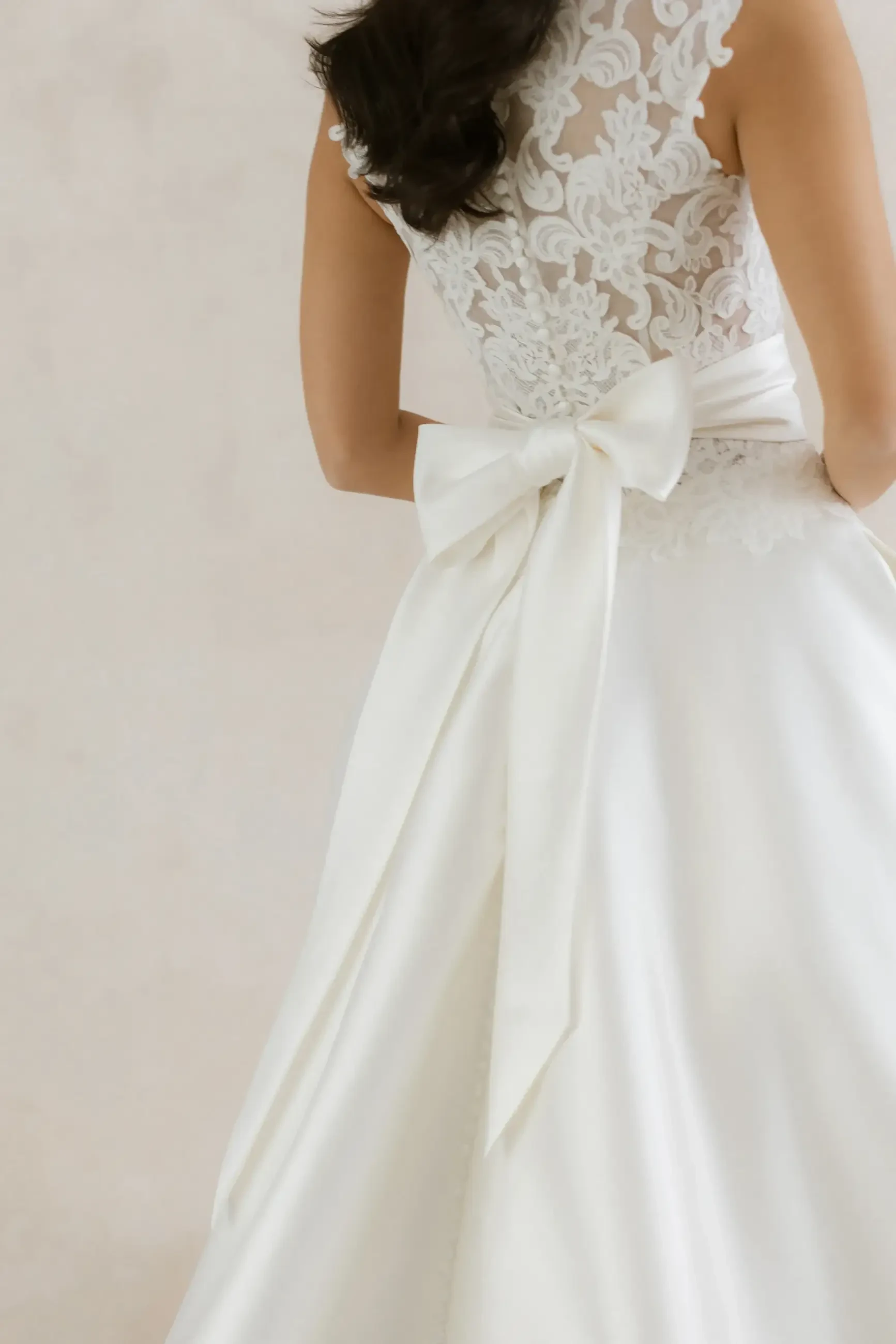 model is wearing a sleeveless a-line wedding dress with a bow on the back