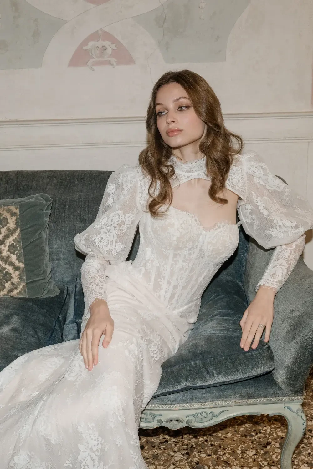 A woman in a vintage lace gown sits elegantly on a couch, displaying an air of sophistication and grace.