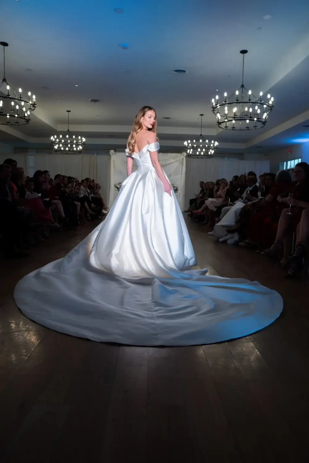 A model walks down the runway in a stunning white gown with a long train during a fashion show.
