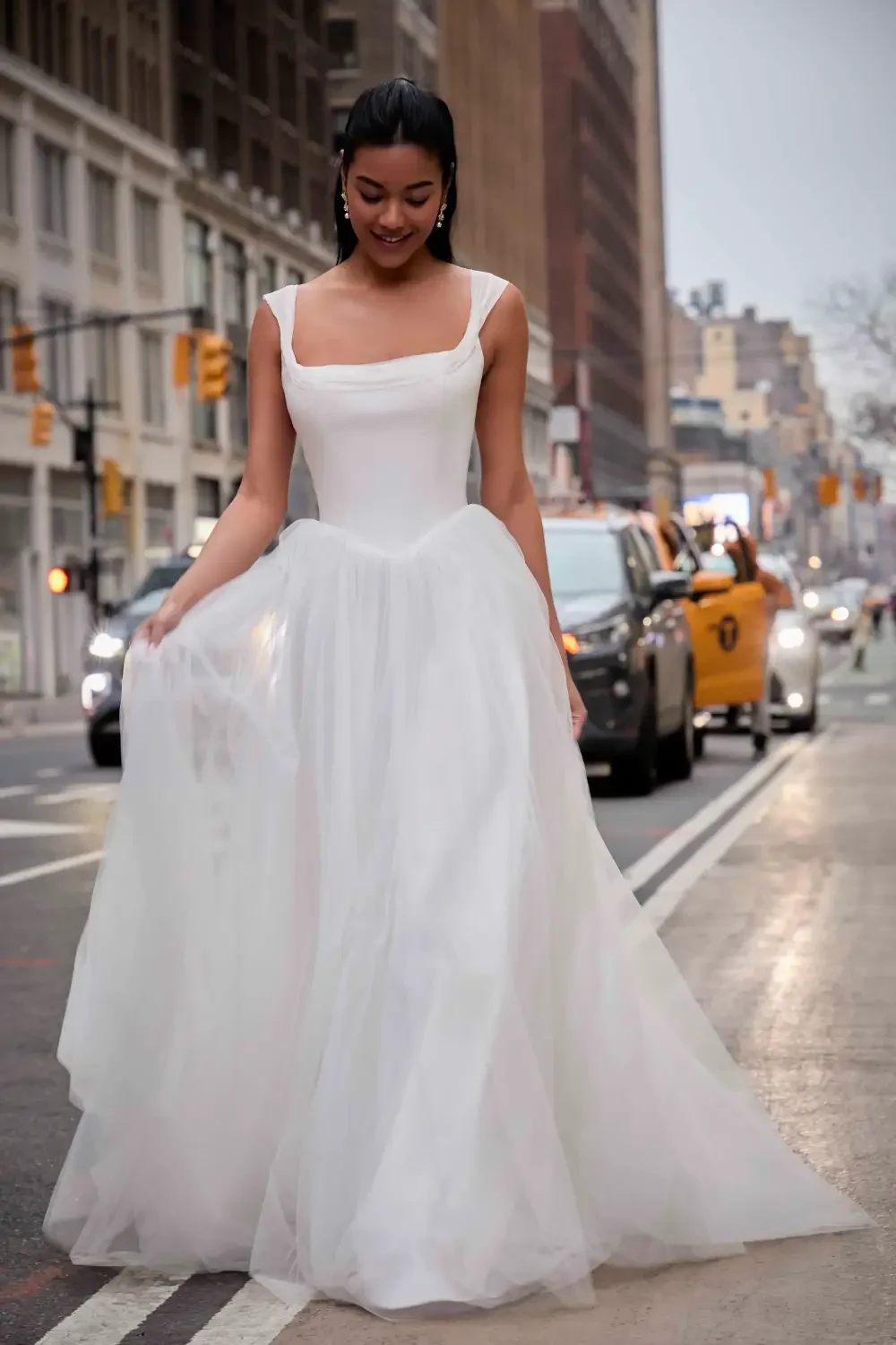 A woman in a white gown walking on a city street with yellow taxis in the background.